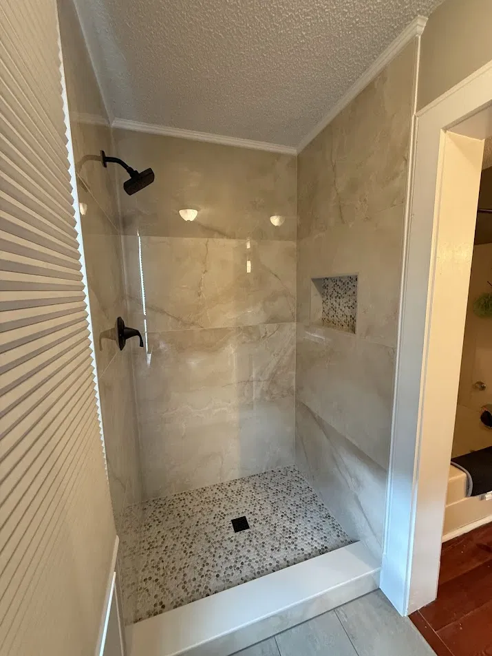 Custom shower with large format marble tile, penny tile floor, and built-in niche by CNB Renovations